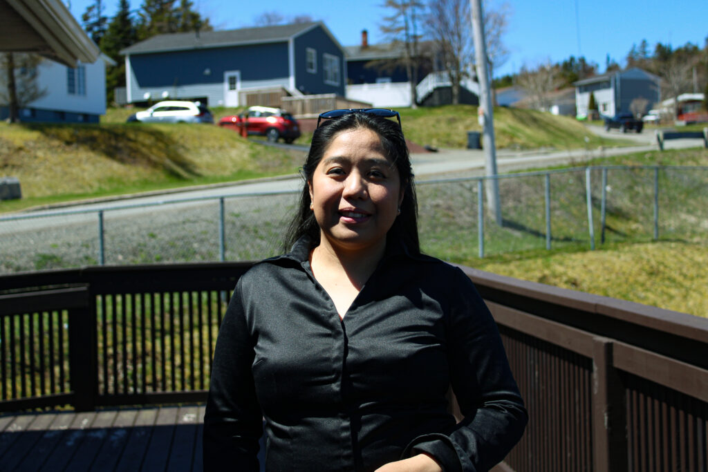 A woman in black shirt stands and smiles in a patio.